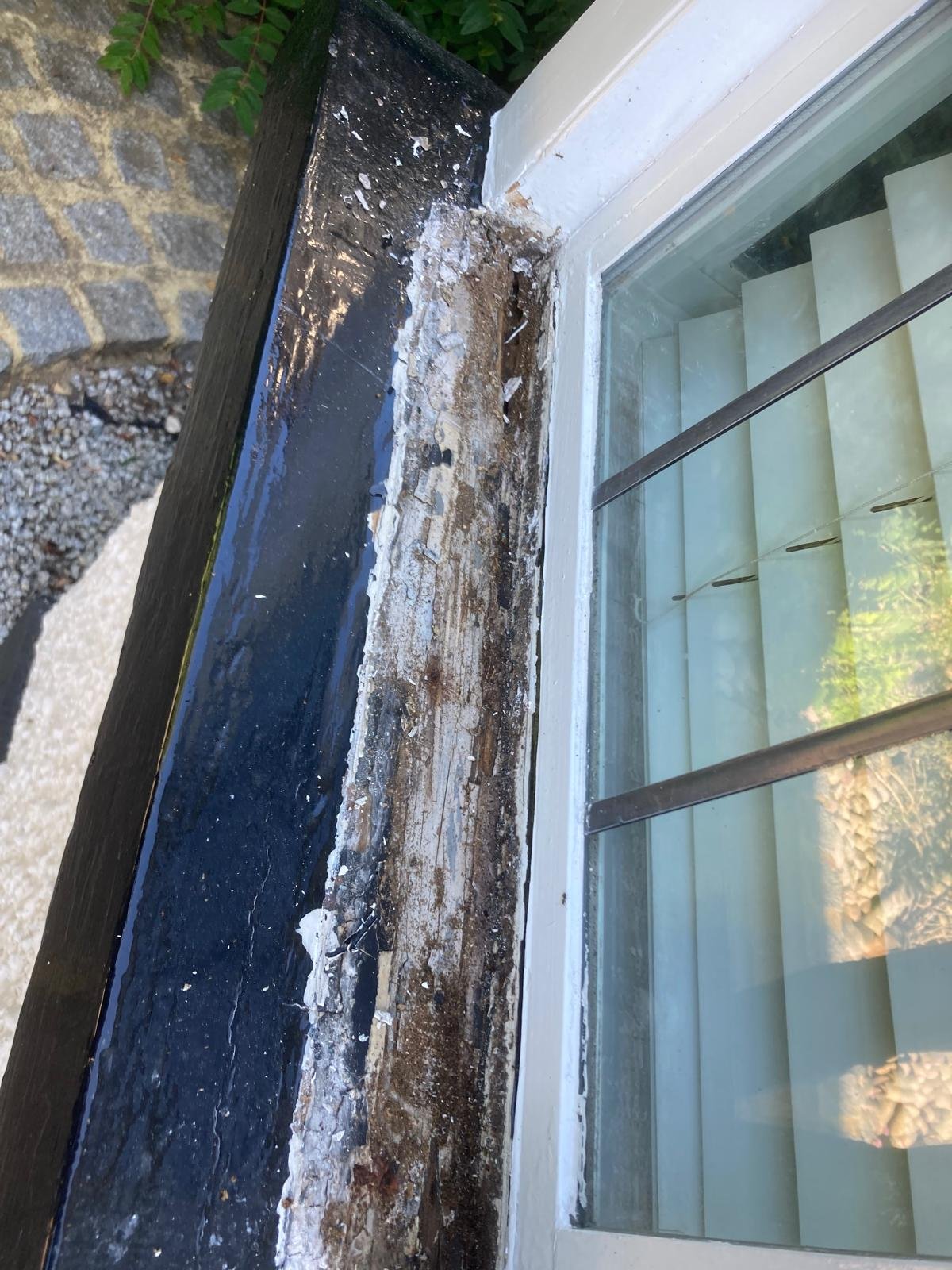 Rotten window sill top hidden under black gloss paint