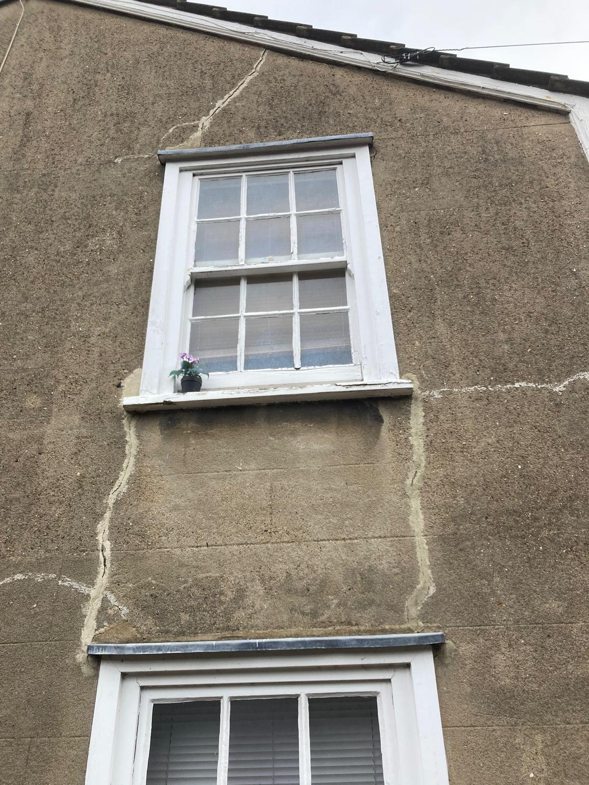 Cracked, stained render and weathered sash windows on the cottage gable before work started