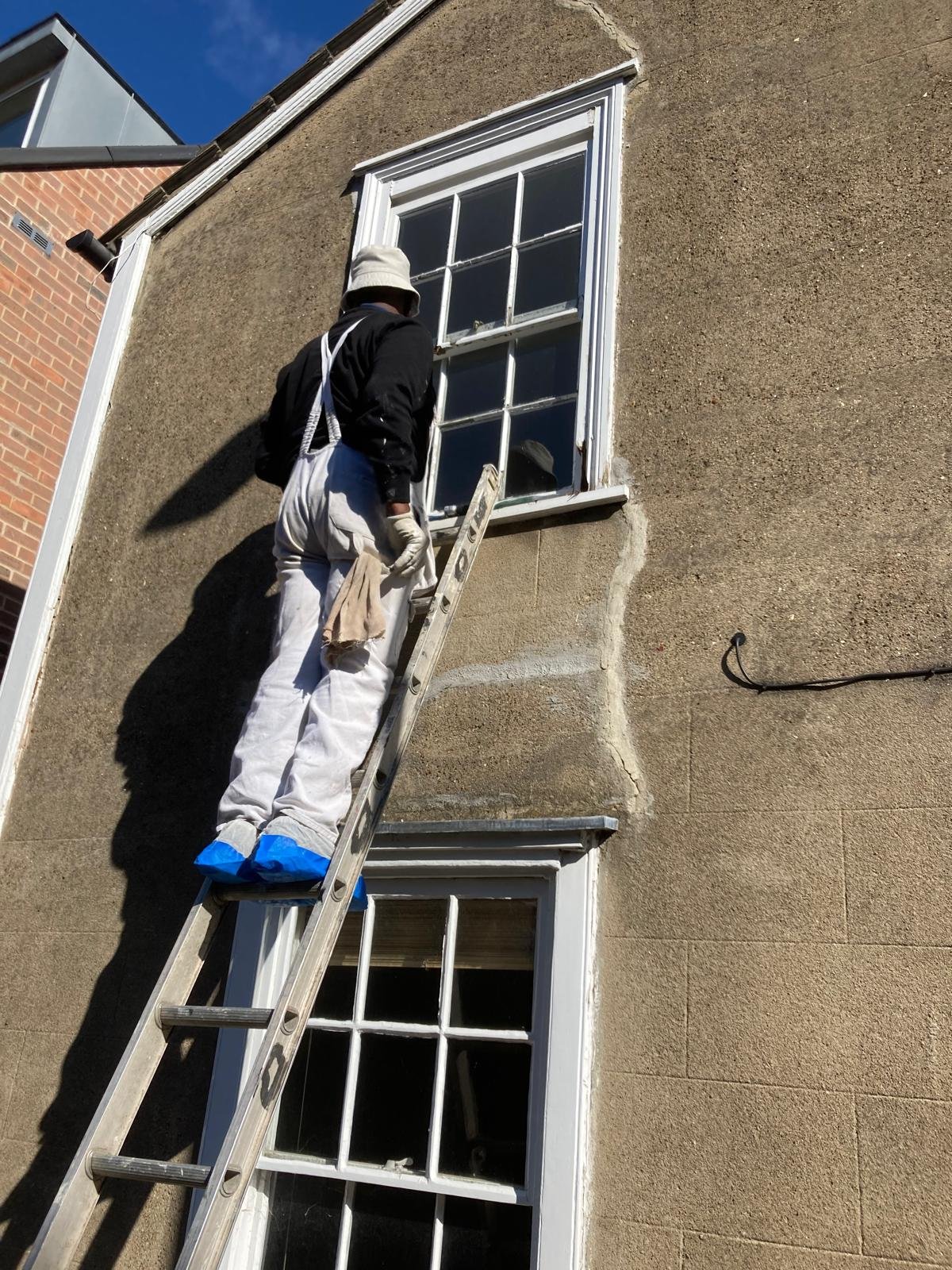 Decorator on a ladder repairing an upper sash window