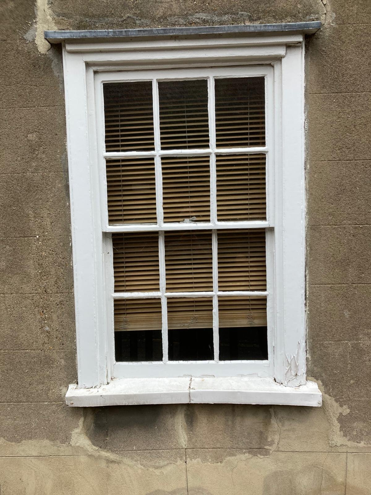 Weathered ground-floor sash window with flaking paint before repair